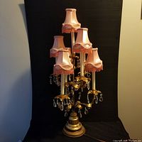 Full view of vintage French style candelabra with six candle lights with pink fabric shades and crystal prisms, gold-tone metal body with leaf motif base