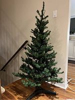 Assembled artificial 4.5 foot Christmas tree with green pine needles and black stand in a home environment.