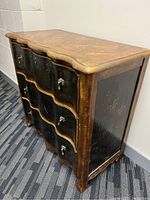 Front and right angled view of antique style wood dresser showing wave edged top and curved front drawers with brass handles.
