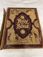 Front cover of antique Victorian era leather bound Holy Bible with gold embossed illustrations and title.