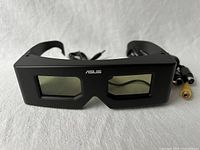 Front view of black ASUS VR 100G LCD 3D glasses showing rectangular tinted lenses and wires coming out from the side.