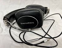 Front and side view of headphones with visible Bowers & Wilkins logo and attached audio cable showing the jack plug.