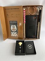 Harley Davidson 105 Years anniversary gift set components including copper cuff bracelet, leatherette folio, keychain, mini flags, and admission card inside golden box.