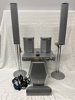 Full view of surround sound system components including floor speakers on stands, bookshelf speakers, AV receiver, center speaker, subwoofer, remote, and cables.