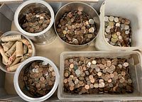 Eight pre-rolled penny rolls alongside five metal and plastic containers filled with loose coins