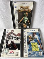 Front view of three Sega Saturn game cases: Tomb Raider, NBA Live 97, and Break Point Tennis, showing cover art and branding.