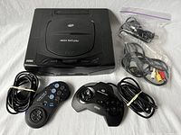 Overview of Sega Saturn console, two controllers and cables on white background