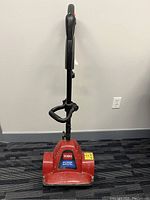 Full front view of the red Toro Power Shovel standing upright on a carpeted floor, showing handle and base.