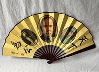 Front side of the fan showing three oval color portraits of important Revolutionary China leaders with Chinese calligraphy characters printed on a yellow background and mounted on dark wooden ribs.