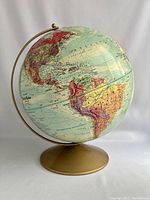 Photo of globe showing North and South America with raised relief details and mounted on gold-colored base.