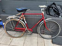 Side profile view showing the full red Raleigh Transit bicycle with single speed setup, rear rack and chain guard.