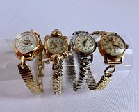 Four vintage ladies' windup cocktail watches resting on clear display stand showing varied case shapes and band materials