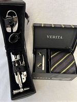 Wine accessory set including corkscrew, foil cutter, and bottle stopper in black case next to boxed striped tie, cufflinks, and tie pin set