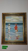 Full view of the framed painting showing two children standing in water at the beach under a cloudy sky.