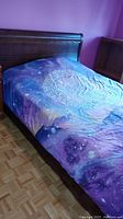 Full view of queen size bed with wooden headboard and mattress covered in celestial-themed bedsheet with galaxy and mandala patterns.