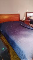 Full view of double bed with wood headboard and dark blue bedding with moon and star pattern, showing bed and part of nightstand.