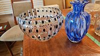 Blue and white swirl glass vase and clear glass bowl with black polka dots placed on a wooden table.