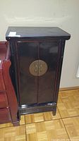 Front view of lacquered wood cabinet showing black glossy finish and brass circular hardware on double doors.