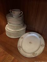 Stack of soup bowls and appetizer plates with a single cup on top, arranged on the floor against a wood-paneled wall