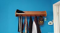 Front view of wooden coat rack mounted on a blue wall with hooks holding coats and hats, shelf with some items on top.