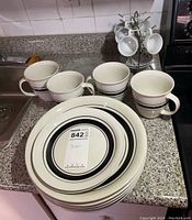 Photo showing four mugs and stacked plates with black ring design.