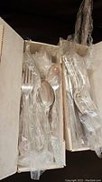 Two boxes of flatware cutlery wrapped in plastic, including forks and spoons.