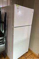 Full view of white Kenmore refrigerator with top freezer and two doors. Visible dent on top freezer door on right side.