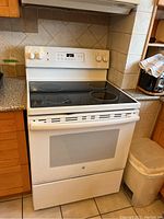 Front view of General Electric white electric stove with glass cooktop, showing four burners and oven door with window.