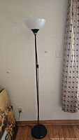 Black floor lamp with white plastic upward-facing shade and metal pole