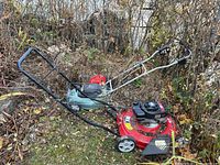 View of two lawn mowers outdoors, showing full units and handles