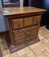 Photo of wood nightstand showing front and left side, polished medium-tone wood, two small top drawers and two large bottom drawers, burn marks visible on top surface