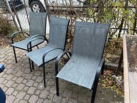 Three patio chairs arranged outdoors on a brick patio, showing overall condition and style