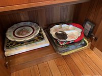 Shelf with mixed serving trays and porcelain plates stacked, includes plastic, metal trays and larger porcelain plate with figure design