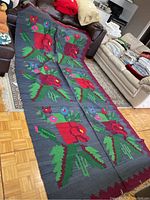 Full view of the large wool woven floral motif rug laid out on the floor showing the repeated red flower designs with green leaves and smaller flowers on a dark gray background.