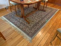 Full view of the rectangular machine woven cotton rug with floral and geometric design placed under a wooden table set on a hardwood floor.