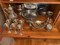 Photo of 18-piece silver plate serving set including tray, goblets, jug with spoon and stand, ice bucket, serving bowl, salt and pepper shakers, and ladle displayed on wooden surface.