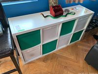White Ikea storage cabinet with a mix of green and white fabric bins, shown from the front with some items on top (not included).