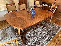 Angle view of the wooden dining table showing the top surface with wood grain and two glass decorative items. Four chairs surround the table.
