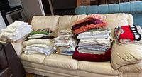 Full overview of the assorted folded tablecloths and curtains on a couch in various colors and patterns.
