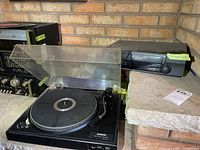 Black Audio Reflex DD-210 direct drive turntable with tonearm and open dust cover, shown alongside the VCR.