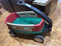 Child's plastic Little Tikes wagon showing red, beige, and green panels, black handle and wheels.