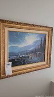Framed "Dawson Yukon River" by Thomas Kinkade painting on wall with detailed carved gold frame and visible label plaque.