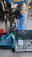Camping gear including folding chair, cooler bag, hammock tent rolled and wrapped in plastic, and propane stove