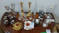 Full view of candle holders on table with assortment of glass, brass, ceramic, and decorative holders visible.