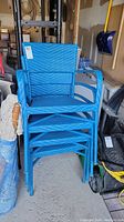 Stack of four blue wicker garden chairs with metal frames, stored in a garage or storage area.