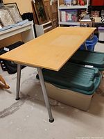 Photo of the wooden desk/table showing the natural wood top and angled metal legs from a corner angle.