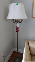 Full view of the metal base floor lamp, showing two pink glass ball accents and white shade next to a beige sofa.