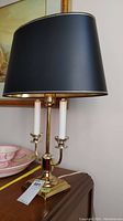 Front view of tri-light brass table lamp with white candle-style bulb holders and a black lampshade with gold lining.