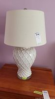 Front view of one ceramic lamp showing crisscross pattern on the base and beige fabric shade.