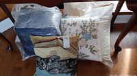 Set of 8 assorted pillows including a cat print pillow, embroidered floral pillow, blue fabric pillows bundled in plastic, and others.